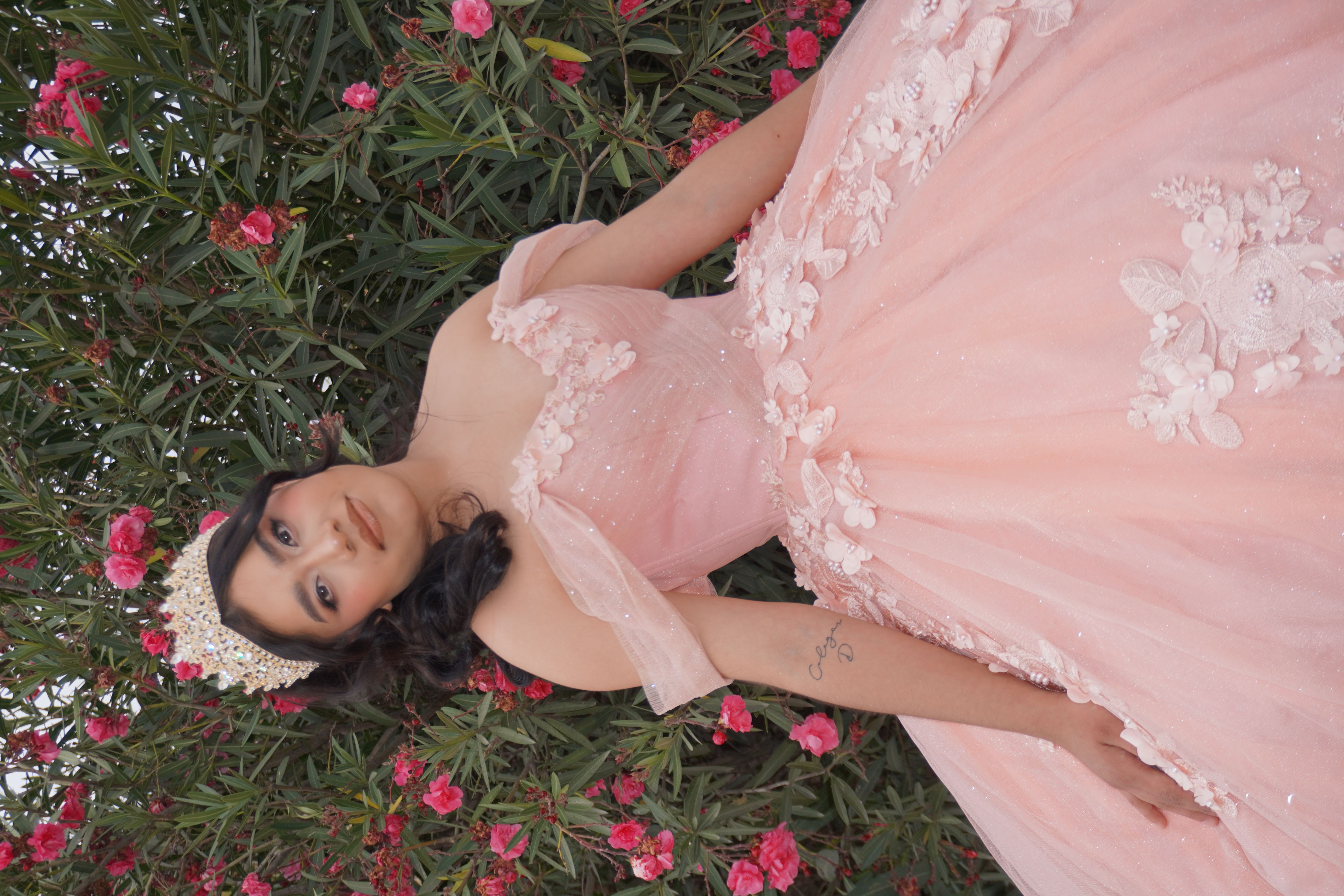 Quinceañera de rosa entre flores rosas con corona dorada