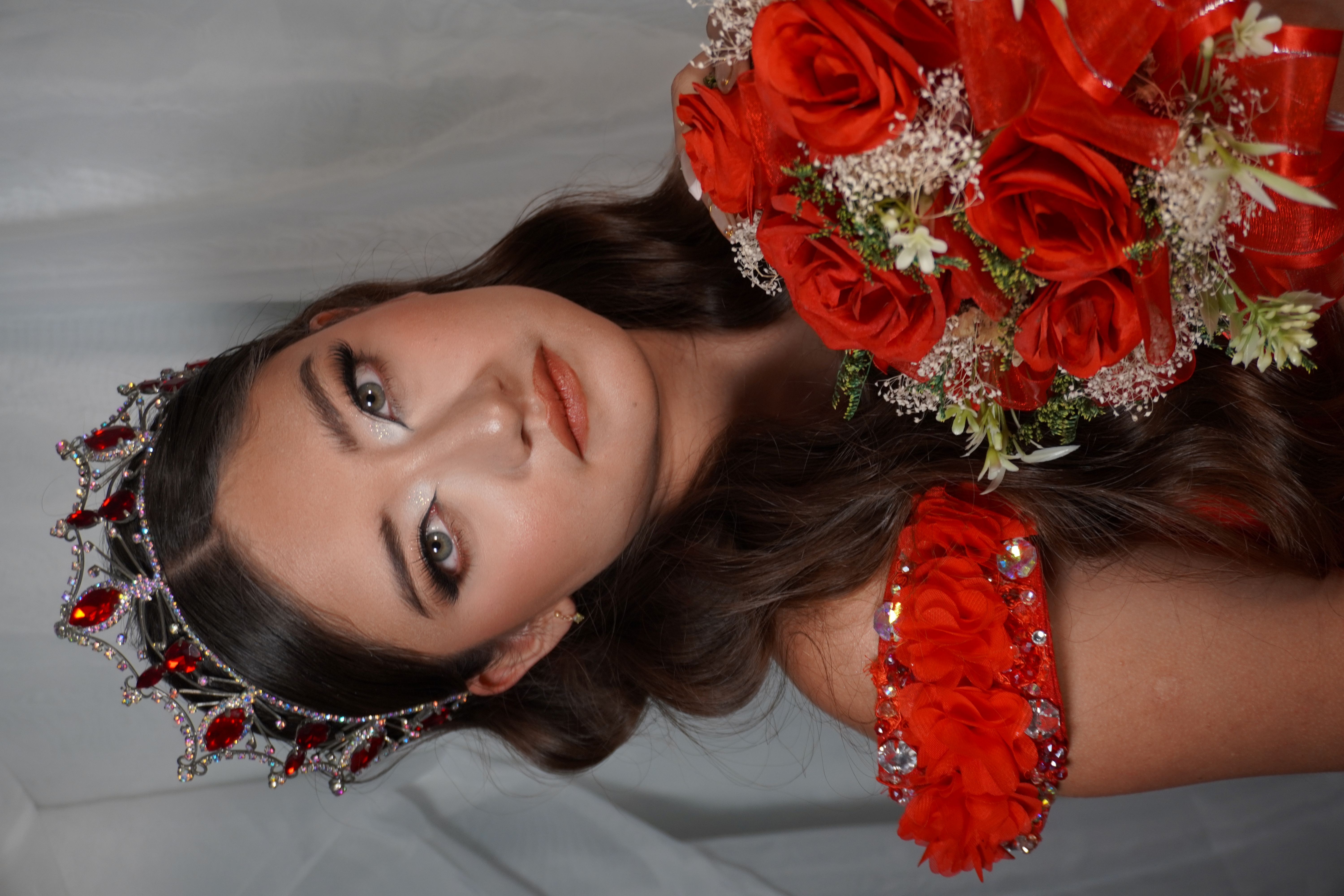 Quinceañera de rojo con ramo de rosas mirando a la camara